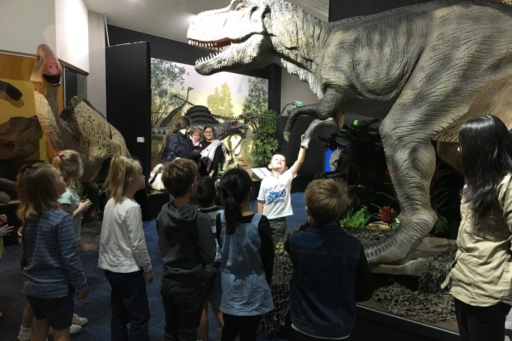 Children and adults observe large dinosaur models in a museum exhibit.